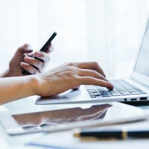 Man inputing data on laptop and holding mobile phone in another hand.